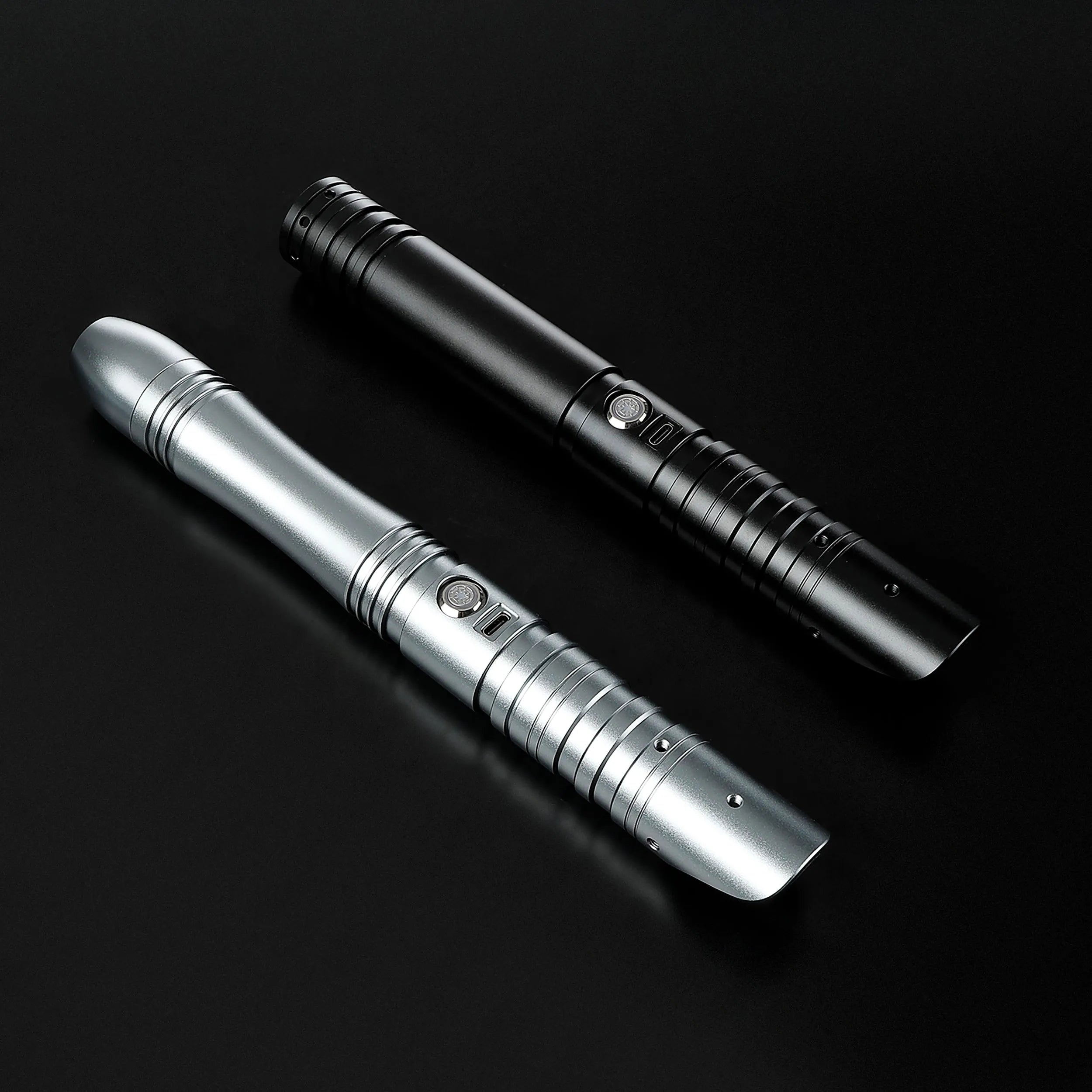 Two aluminum alloy saber hilts, one silver and one black, with ribbed grips and activation buttons.