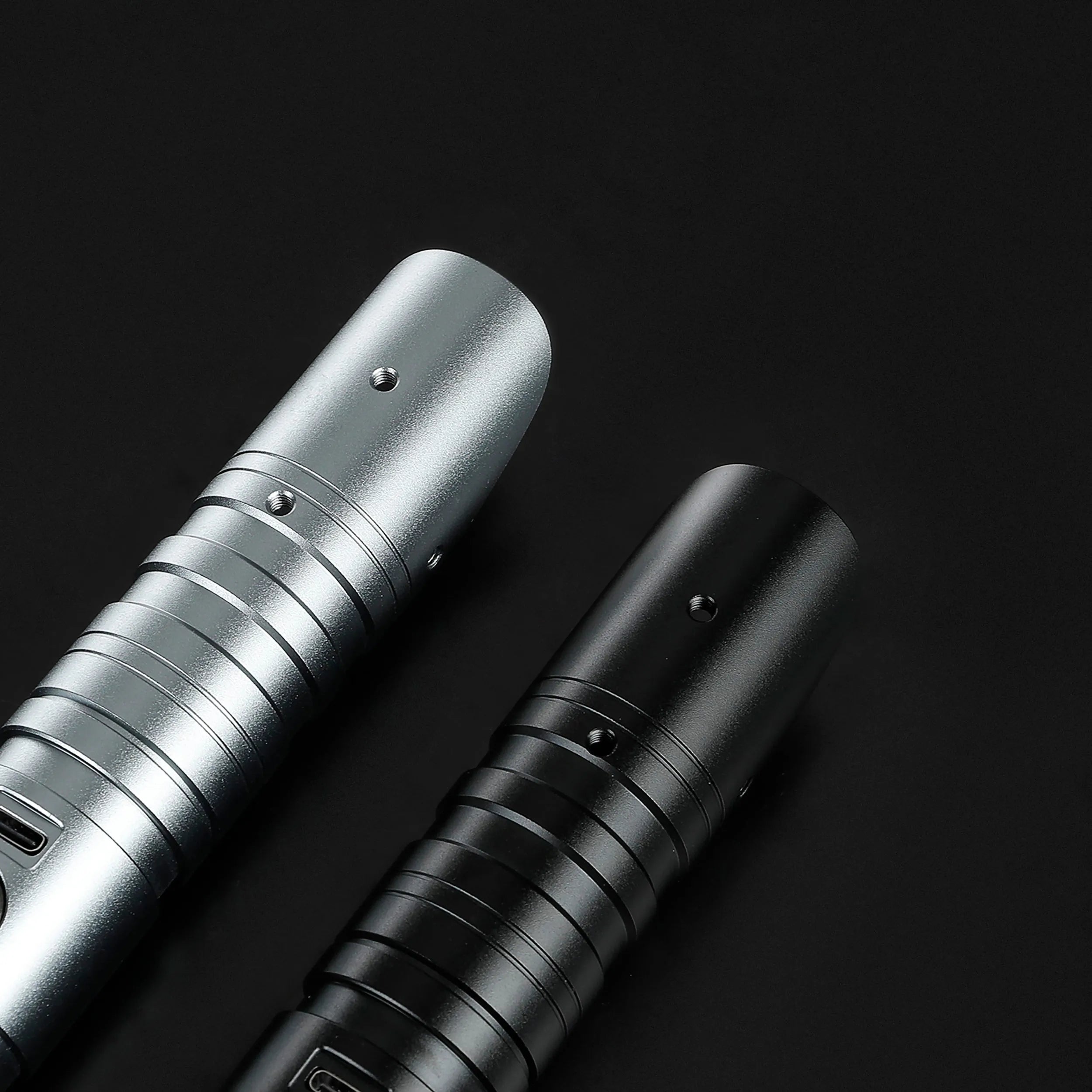 Two aluminum saber hilts, one silver and one black, with ribbed grips and activation buttons.