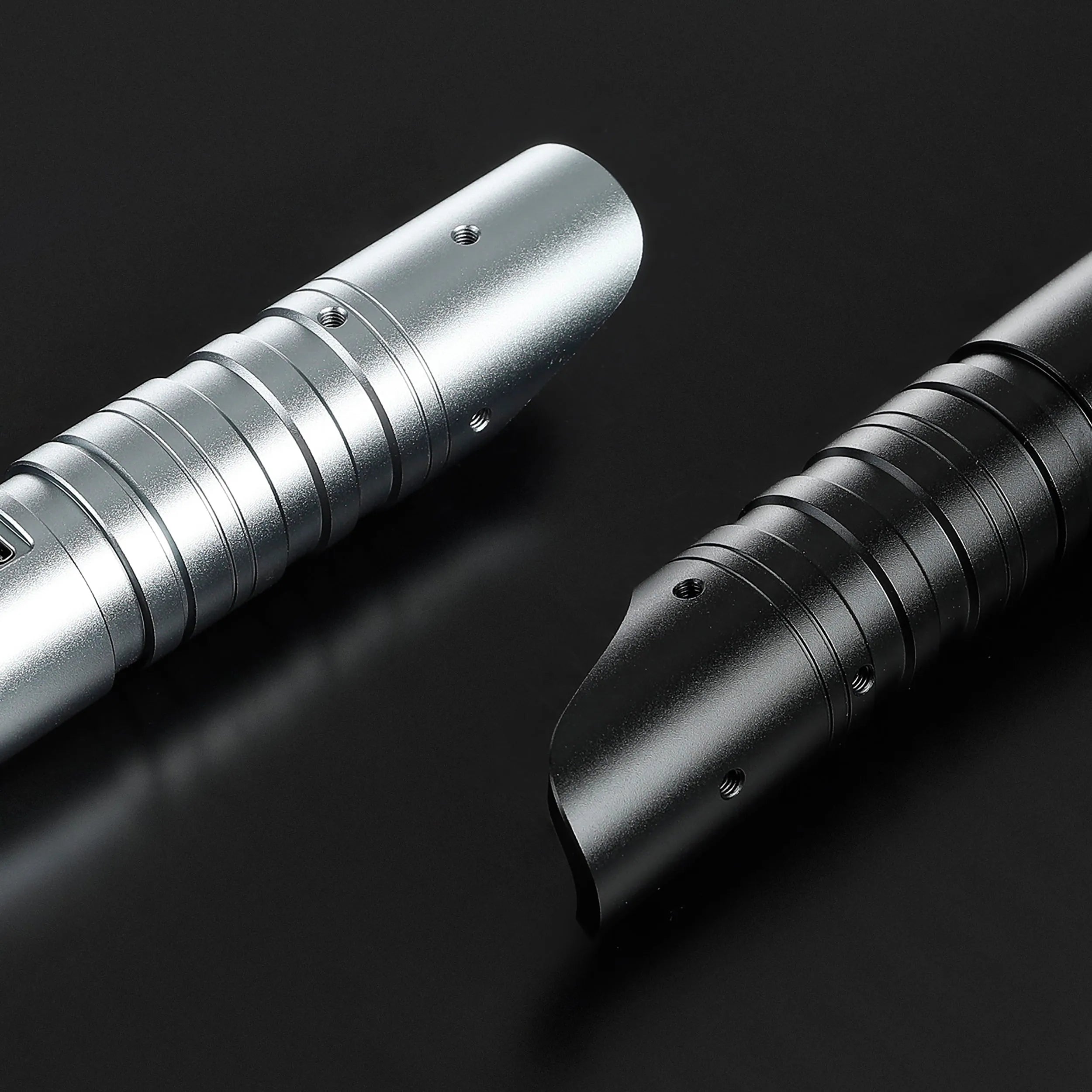 Close-up of two aluminum saber hilts: one silver with ribbed grip, one black with a curved emitter.