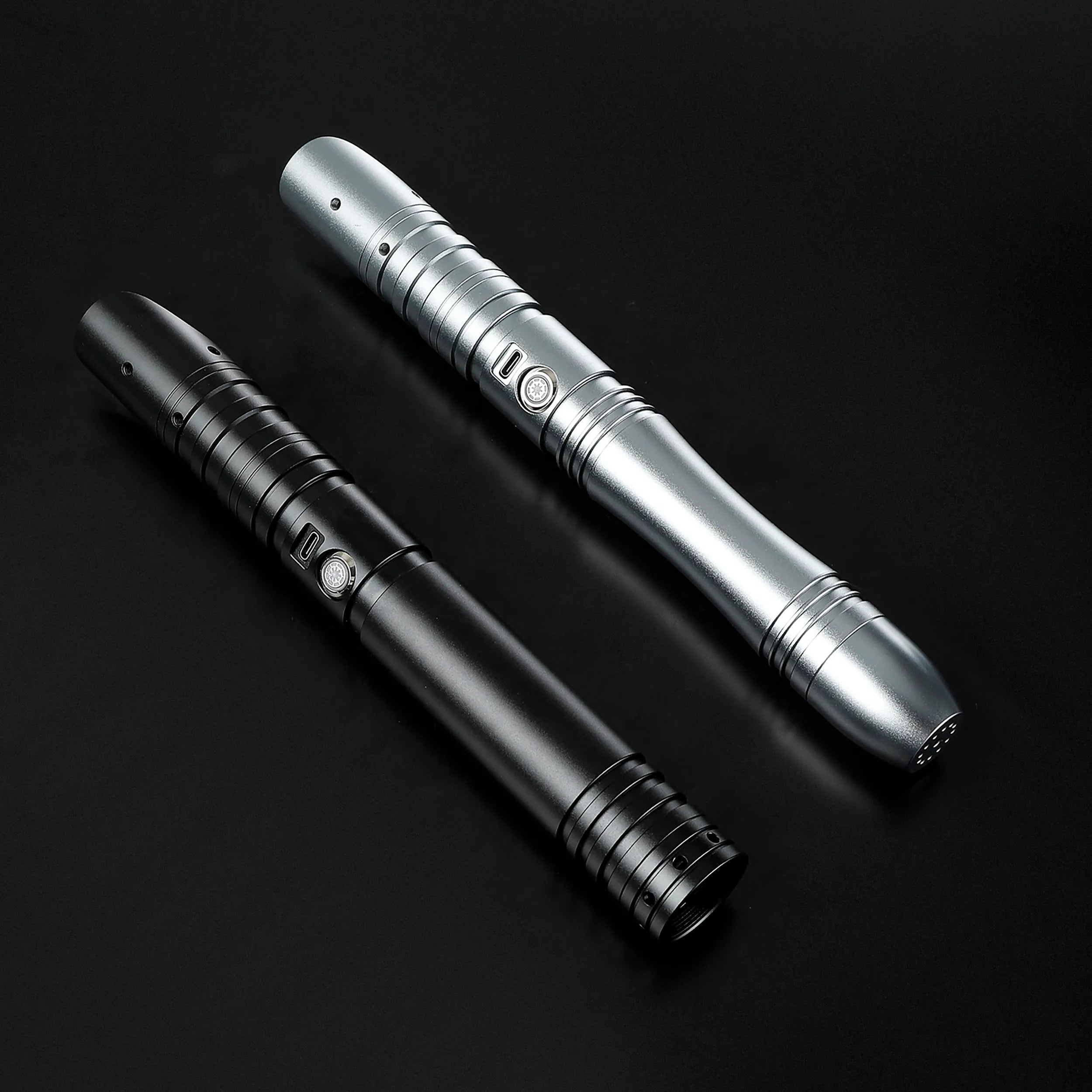 Two sleek aluminum saber hilts, one silver and one black, with button controls and textured grips.