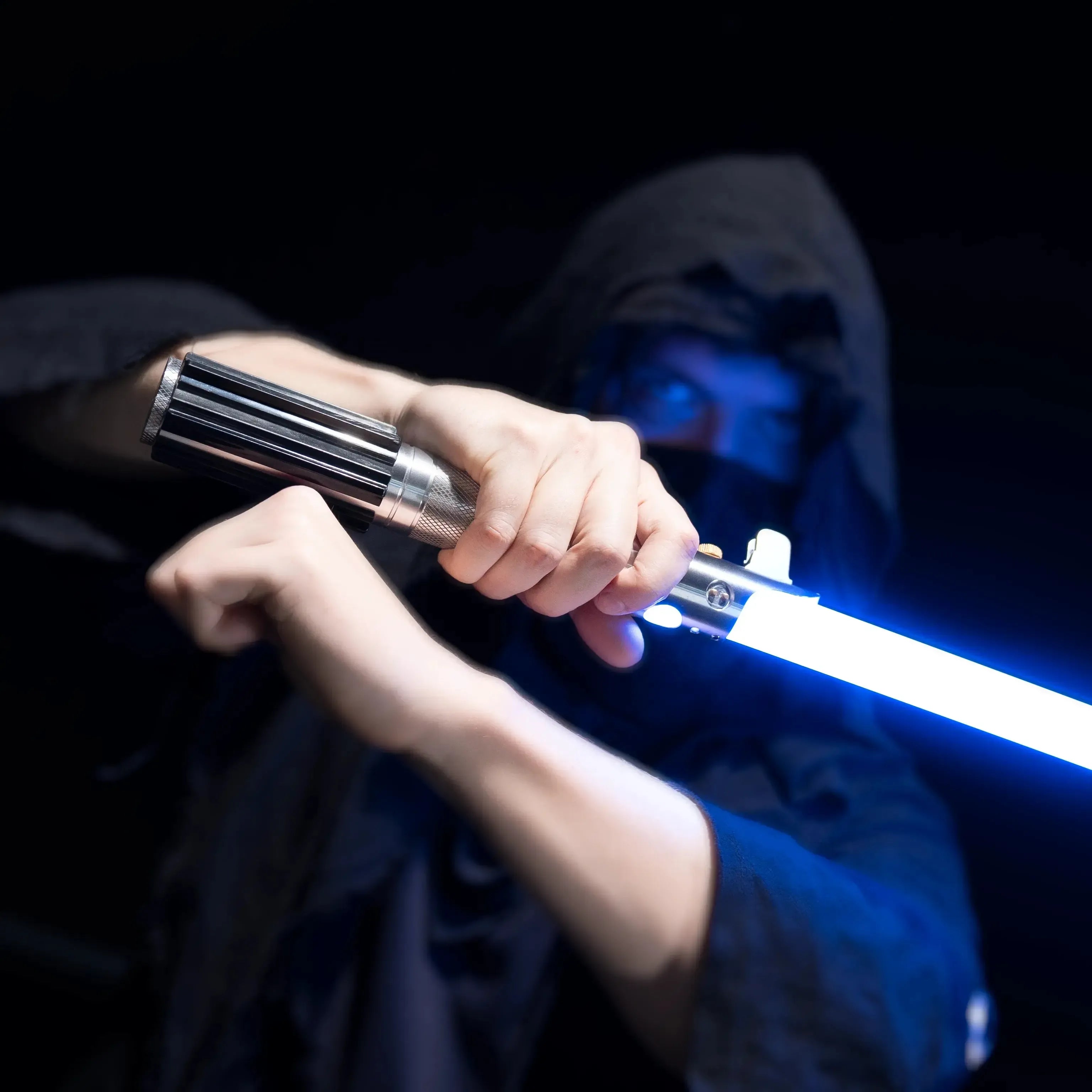 Person in a dark hood holding a glowing blue T6 aluminum alloy Obi-Wan style lightsaber with a sturdy polycarbonate blade.