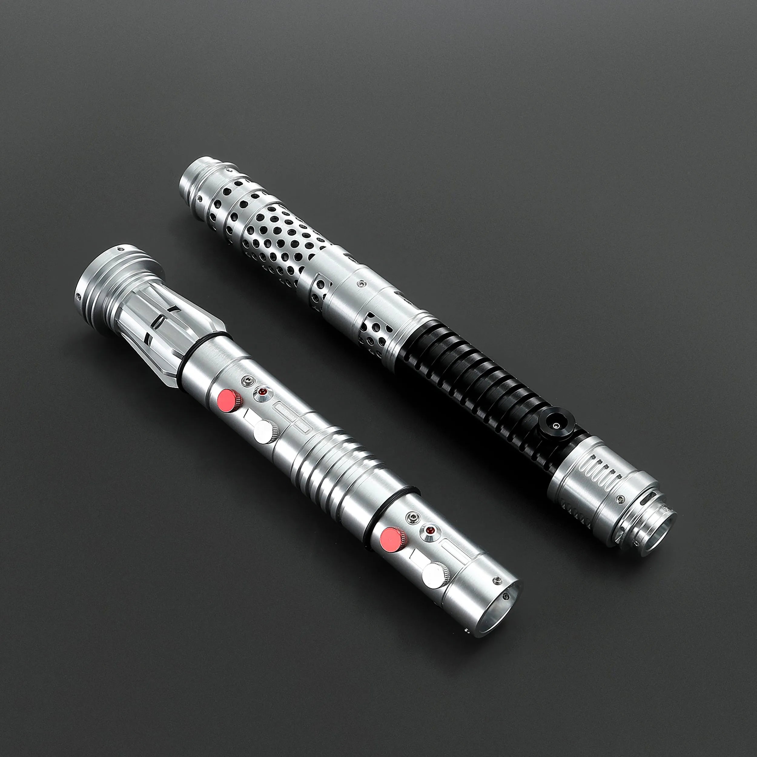 Two brushed silver metal Shadow Lord saber hilts, one with black grip and perforated design, the other with red buttons.