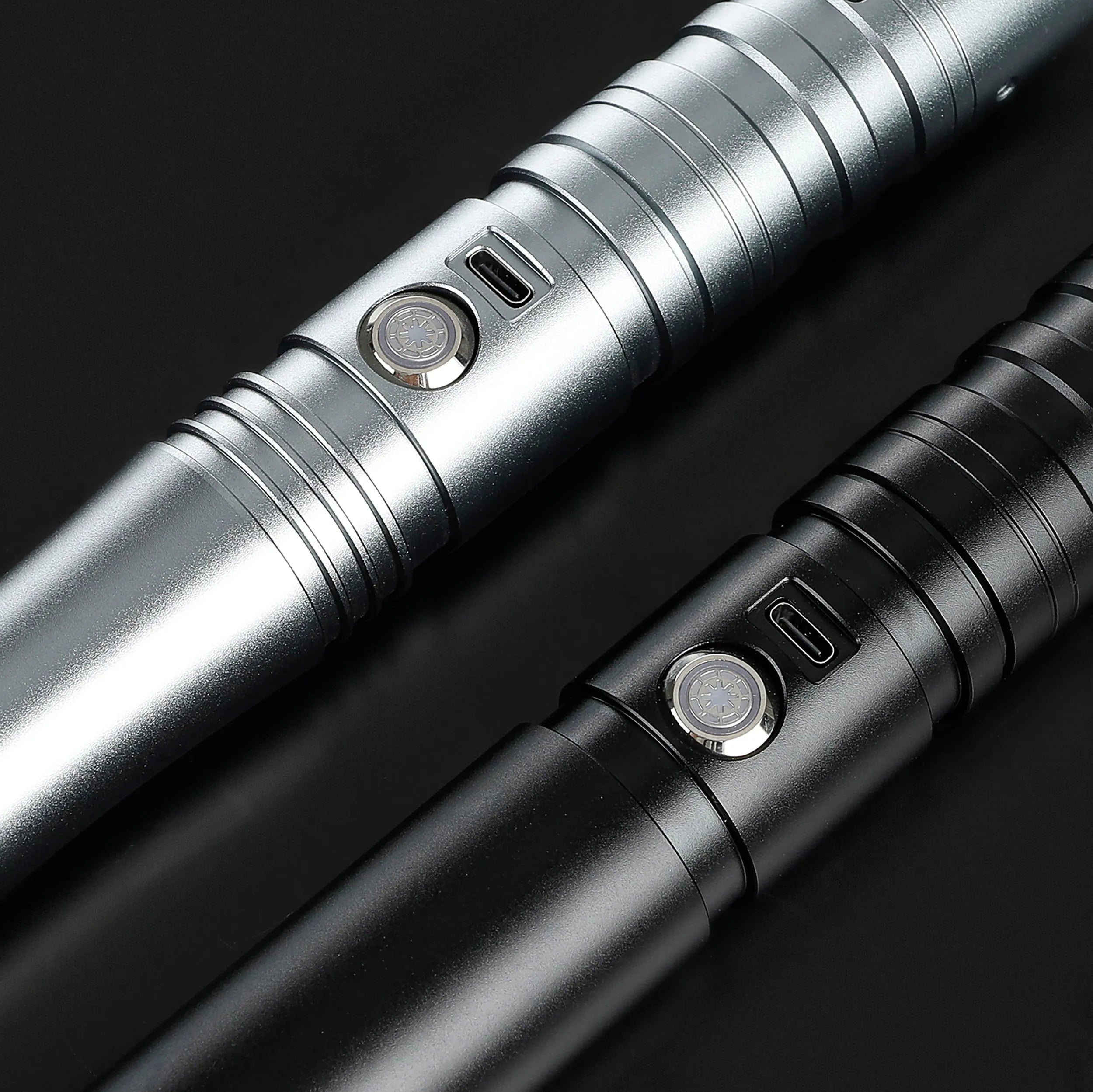 Close-up of two durable aluminum saber hilts, one silver and one black, with activation buttons.