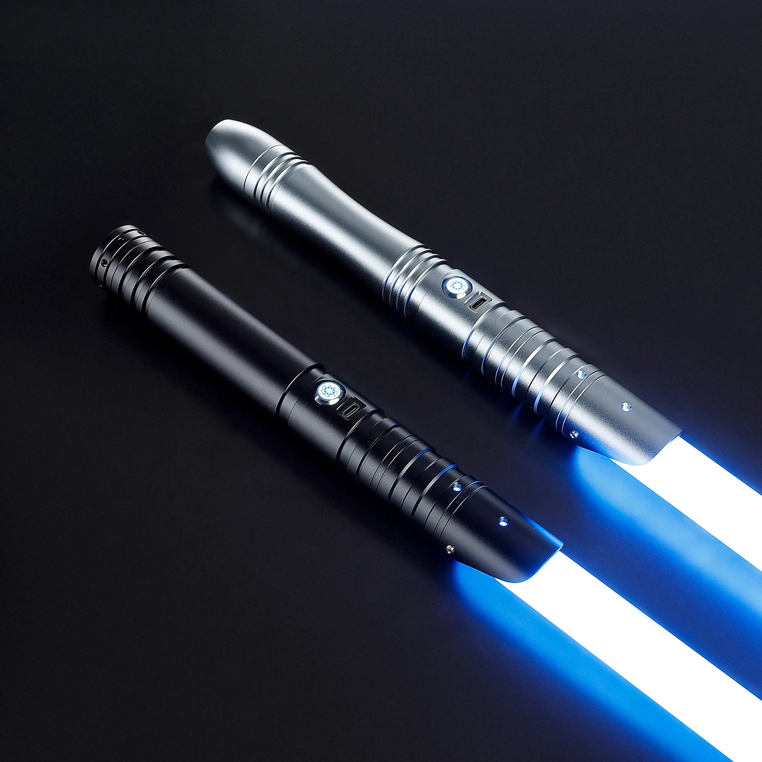 Two baselit sabers with glowing blue blades: a longer silver one and a shorter black one, on a dark background.