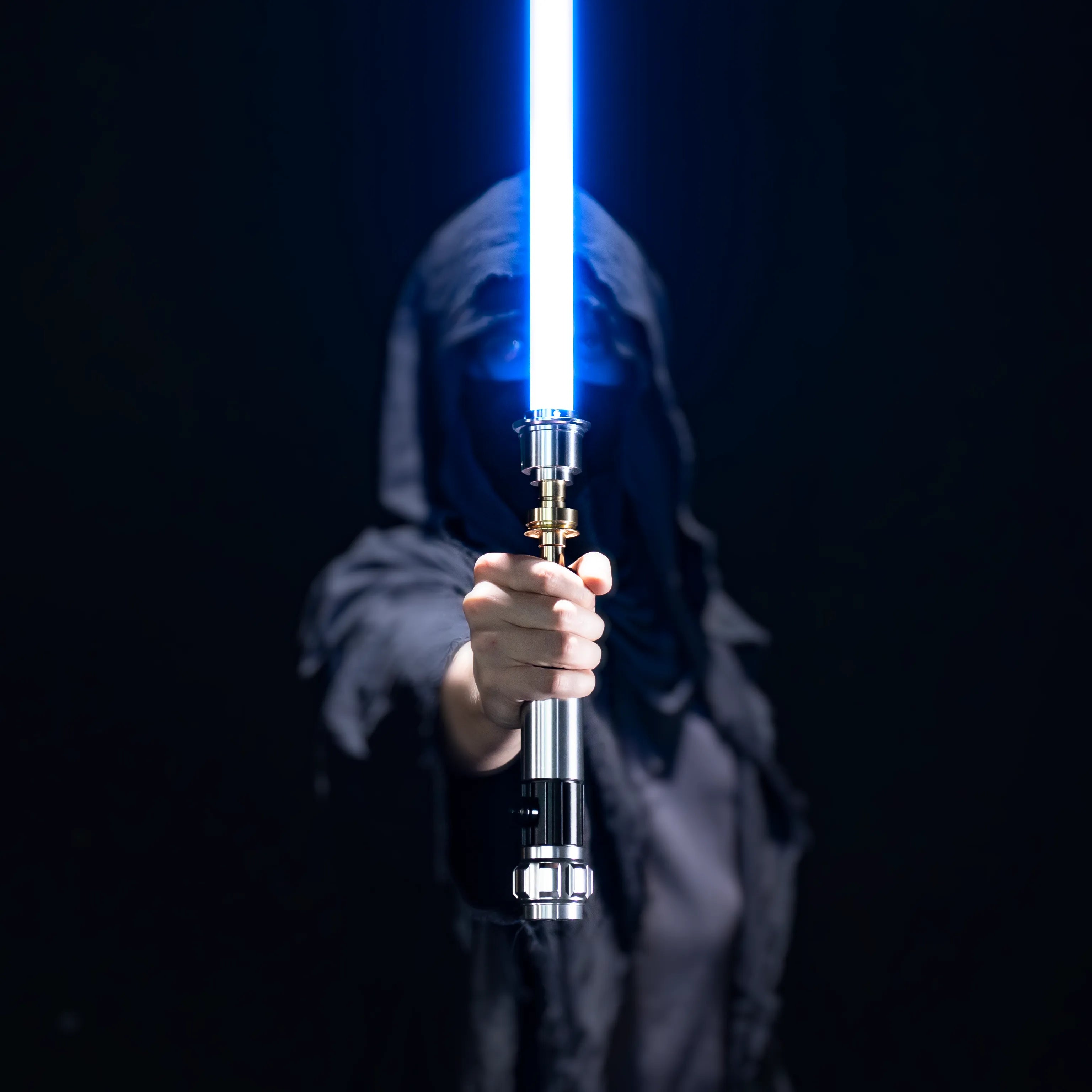 Person in a hooded cloak holding a glowing blue duel-ready aluminum alloy lightsaber against a black background.