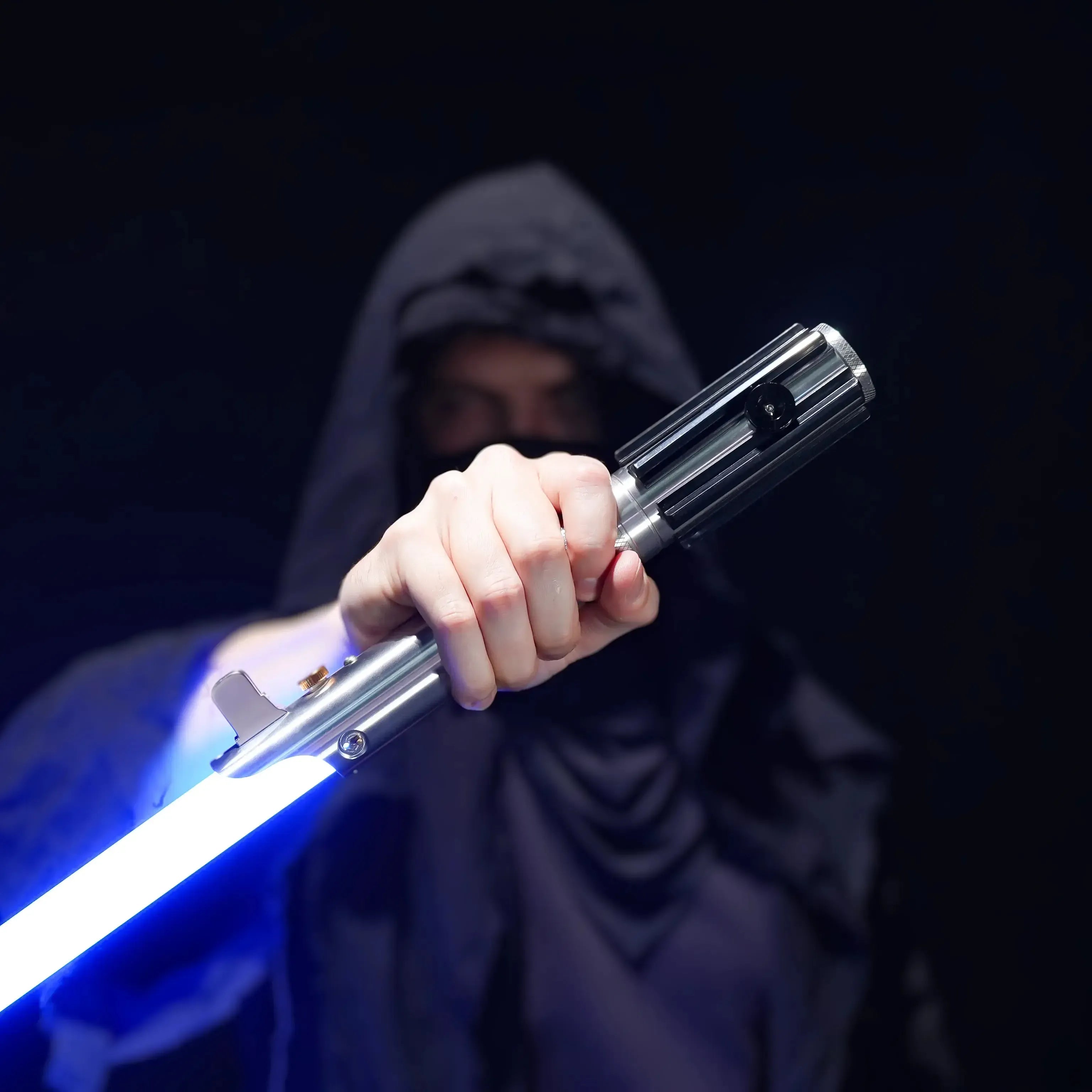 Person in a dark hooded robe holding a metallic aluminum Obi-Wan style lightsaber with a glowing blue polycarbonate blade.