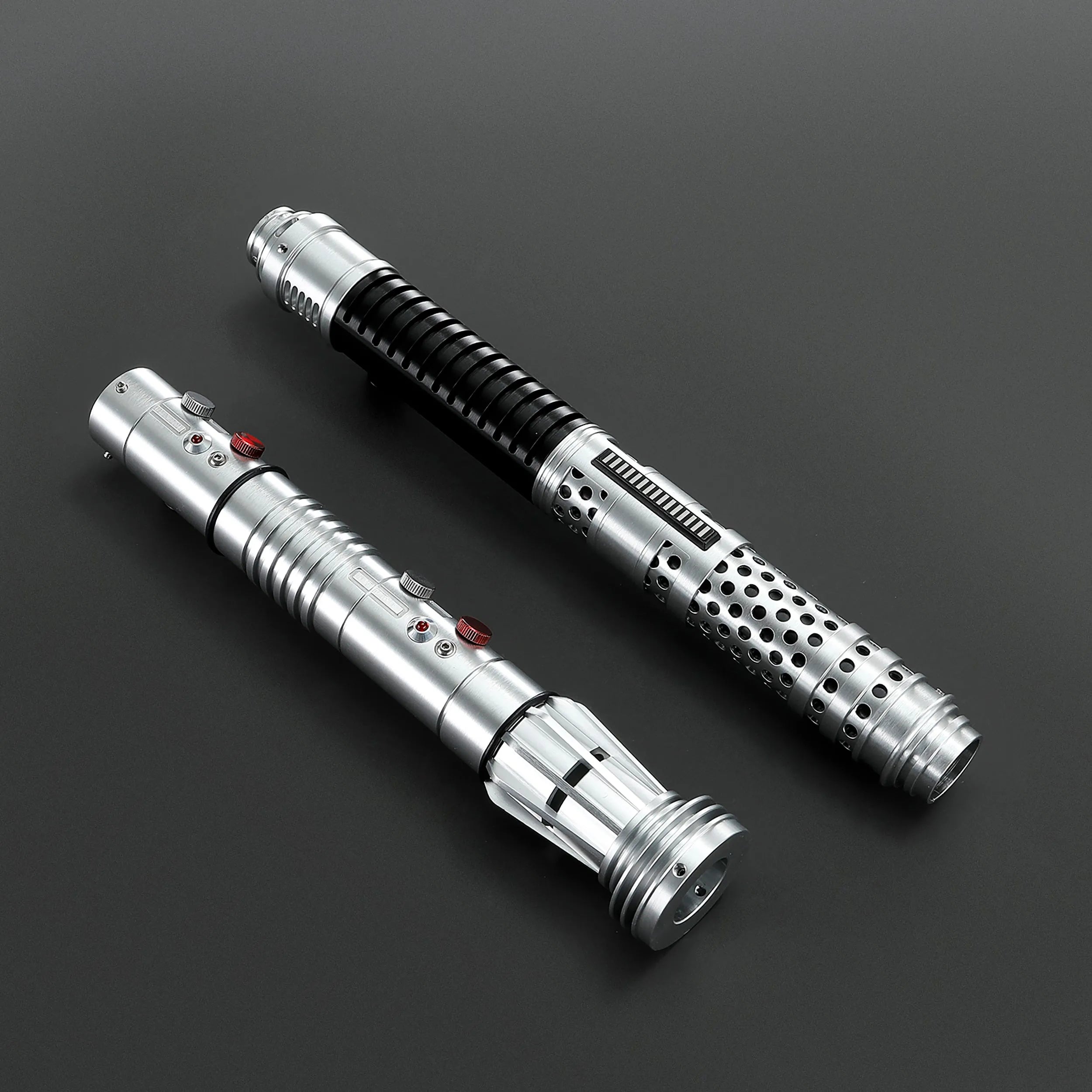 Two brushed silver metal Shadow Lord saber hilts with black accents and red buttons on a dark background.