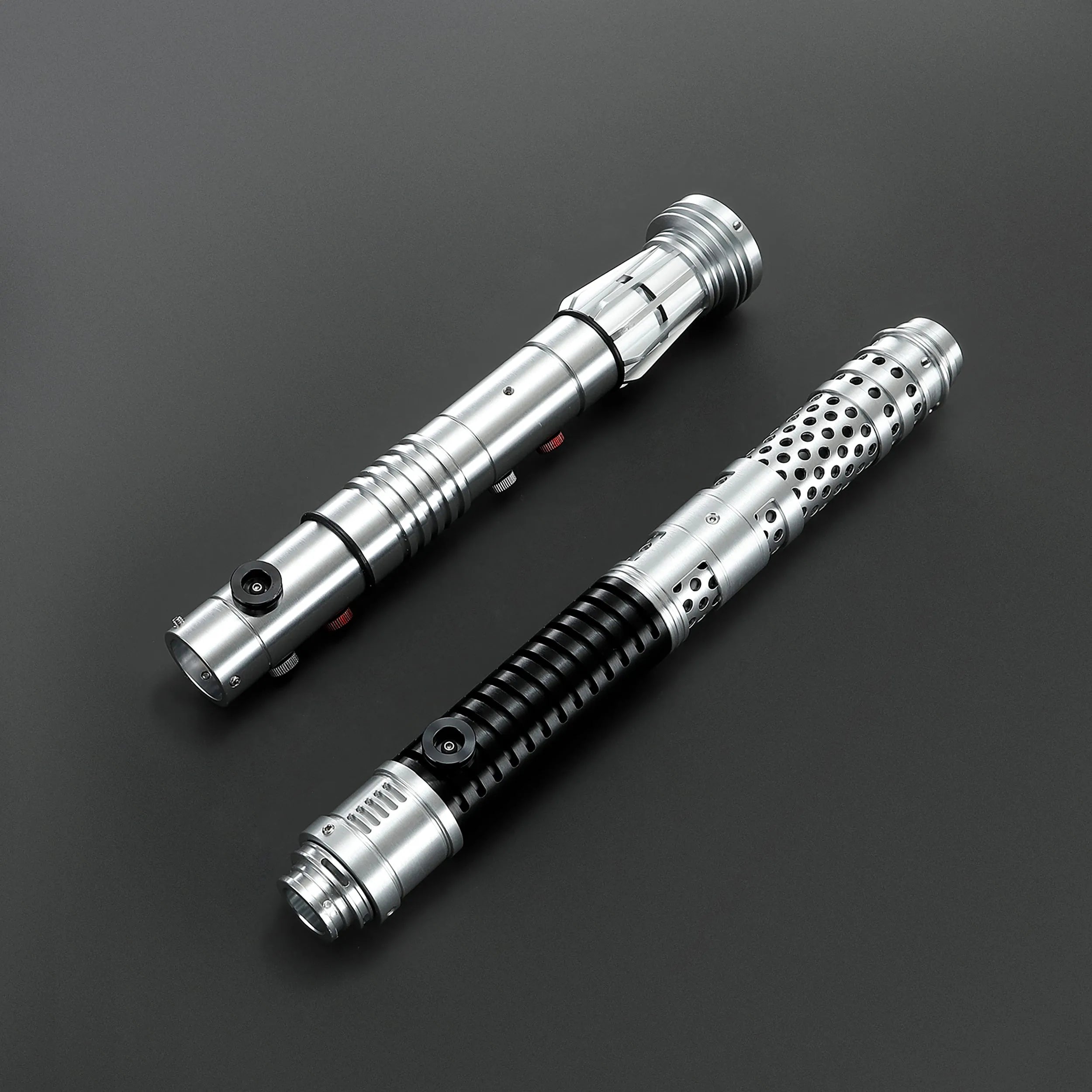 Two brushed silver metal Shadow Lord saber hilts, one with a black ribbed grip, on a dark background.